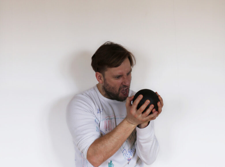 Młody mężczyzna trzyma przed soba czarna kule. Intensywnie się w nią wpatruje i krzyczy.