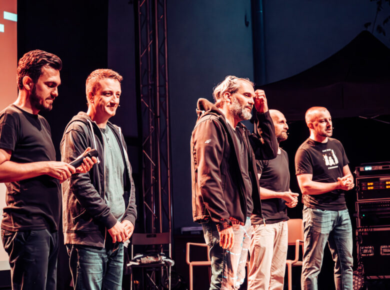 Grupa mężczyzn stoi obok siebie na scenie i rozmawia z publicznością.