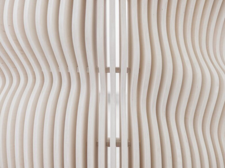 Na zbliżeniu fragment drewnianego stołu, wykonanego z cienkich drążków w kształcie fali.