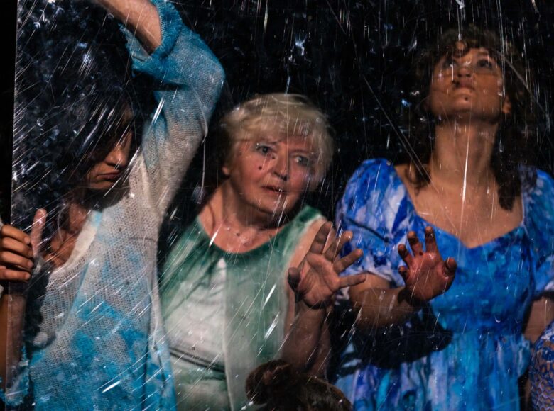 Zdjęcie przedstawia trzy kobiety, które stoją za brudną, podrapaną szybą.