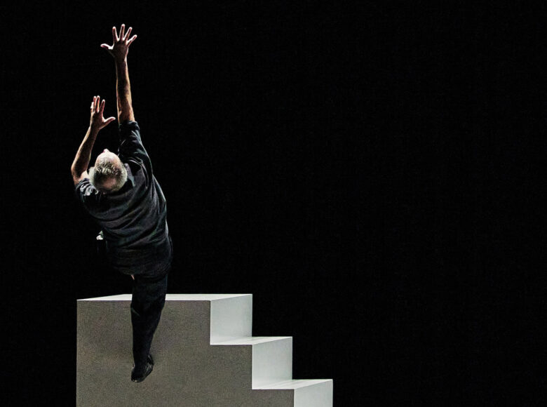 Kolorowa fotografia. Na zdjęciu białe wysokie schody. Na szczycie schodów znajduję się mężczyzna , wygląda jakby miał zaraz z nich spaść.