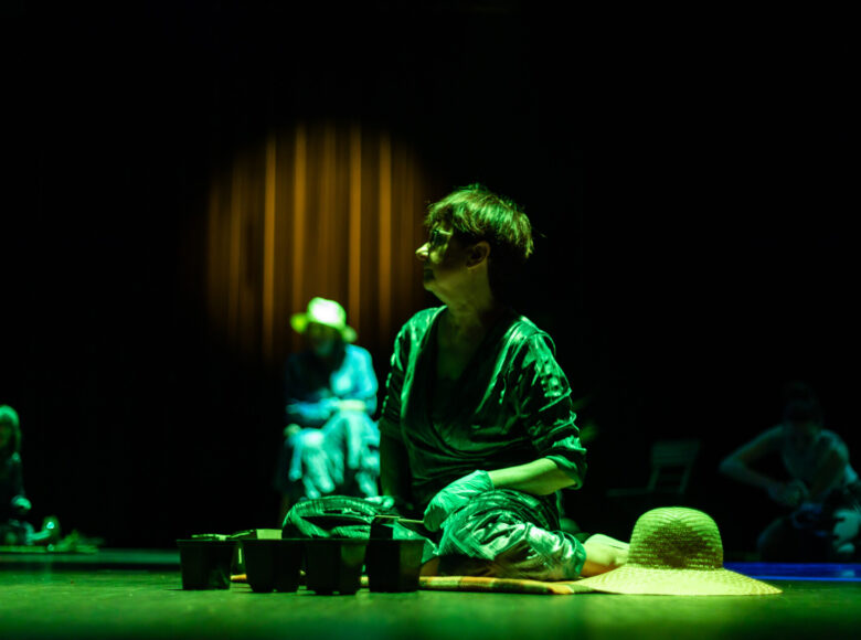 Zdjecie przedstawia kobiety, które siedzą na scenie. Na scenę pada zielone światło.