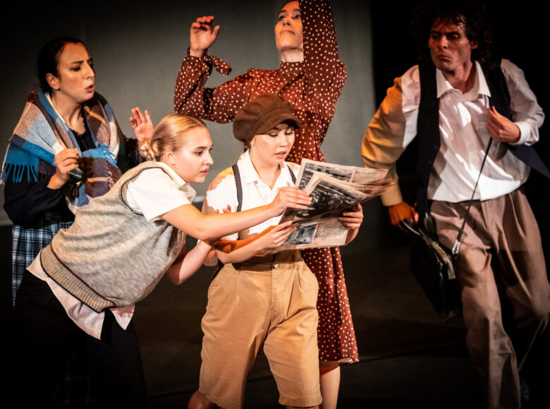 Kolorowa fotografia. Na środku dwie osoby czytają gazetę. Obok przebiega mężczyzna. Z tyłu dwie kobiety wyraźnie czymś zaaferowane.