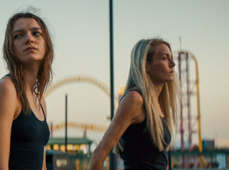 Dwie młode kobiety. Za nimi w tle wydaje się być lunapark i lekko błękitne niebo.