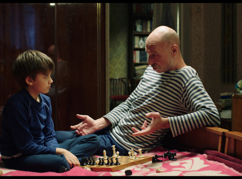 Kadr z filmu. Mężczyzna i chłopiec siedzą na łóżku i grają w szachy.