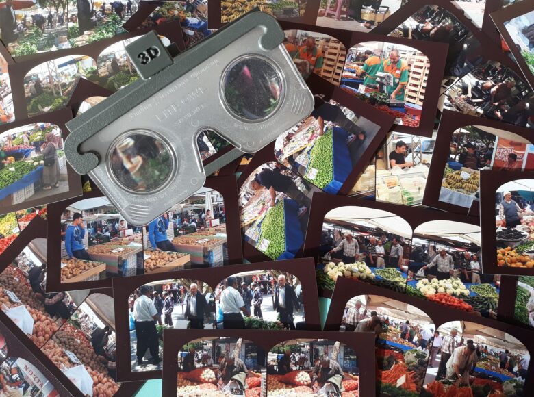 Zdjęcie przedstawia porozkładane na stole fotografie ludzi na targu warzywnym.