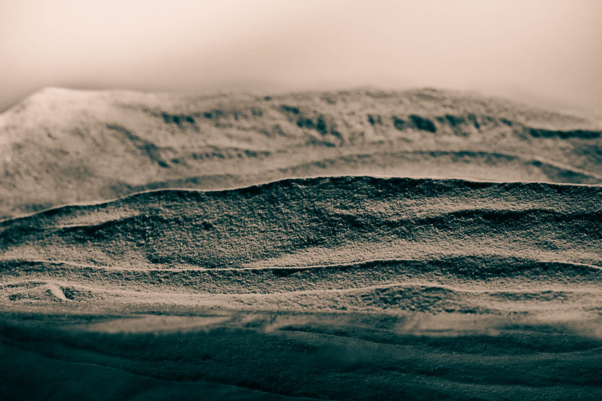 Utrzymana w nostalgicznym nastroju fotografia w sepii, przedstawia pejzaż skalnego płaskowyżu, z zarysowanymi poziomo strukturami równoległych poziomów skał. Niebo nad nimi spowijają fragmenty delikatnych formacji mgły, również w kolorze sepii.