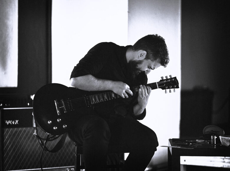 Na zdjęciu mężczyzna siedzący na scenie i grający na gitarze.