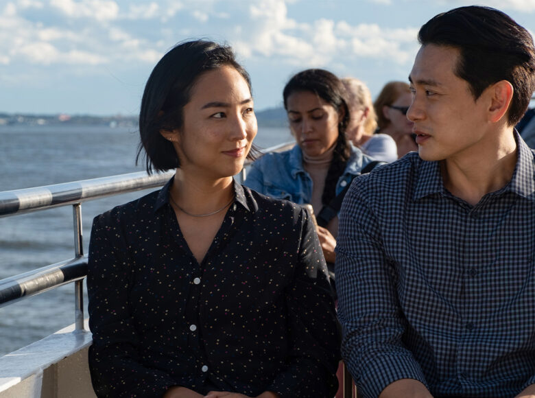 Kadr z filmu. Grupa osób siedzi na pokładzie statku. W tle woda. Na pierwszym planie kobieta i mężczyzna – dwoje młodych Azjatów.