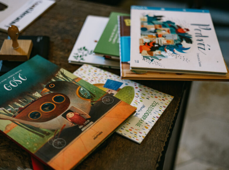 Zdjęcie przedstawia drewniany stolik, na którym lezą książki dla dzieci z kolorowymi okładkami.