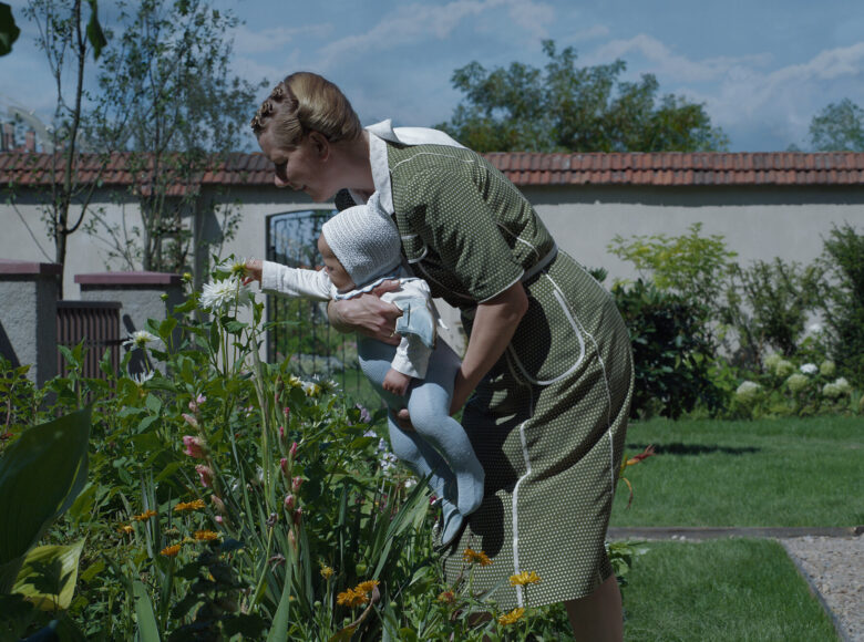 Kobieta trzymająca małe dziecko na rękach pokazuje mu rośliny, pozwala je dotykać. Scena rodzajowa.