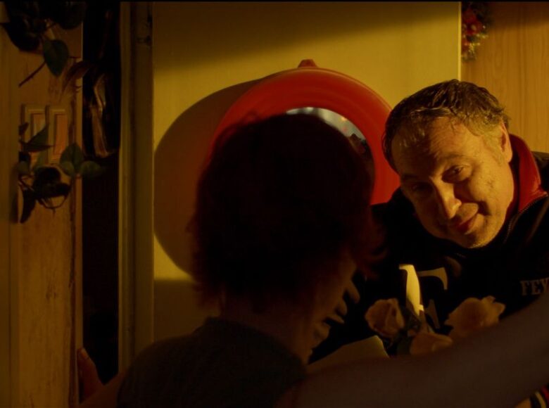 Kadr z filmu. Mężczyzna z bukietem róż stoi w drzwiach do mieszkania, które otwiera mu kobieta.