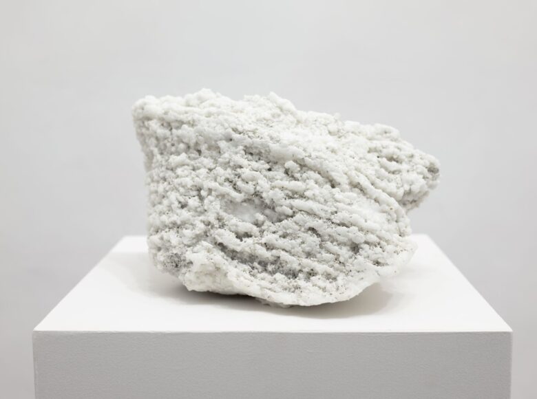 Zdjęcie przedstawia duży, biały, chropowaty kamień, który leży na białym postumencie.