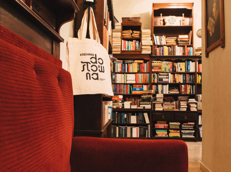 Zdjęcie przedstawia wnętrze księgarni. regały od podłogi do sufitu wypełnione są książkami. Na ścianach wiszą klasyczne obrazy. Na środku stoi czerwona kanapa.