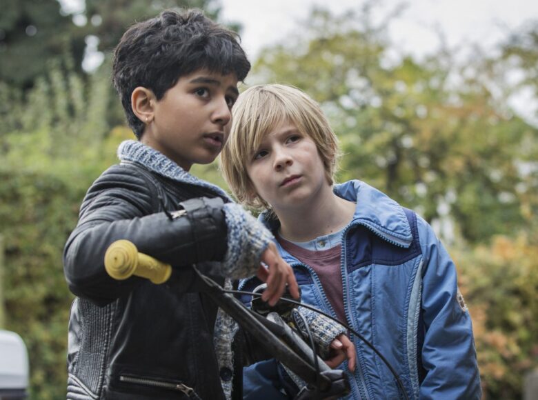 Kadr z filmu. Dwóch chłopców stoi na ulicy i patrzy się nieufnie, jeden z nich oparty jest o ramę roweru.