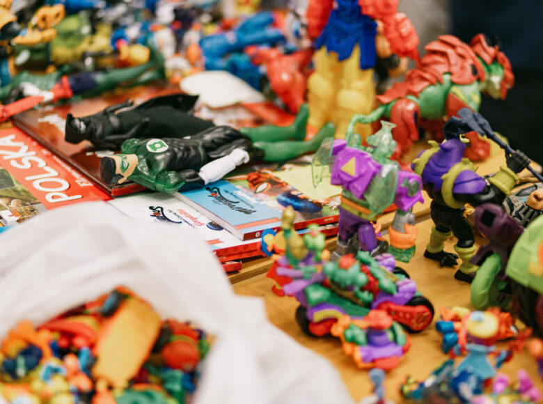 Zdjęcie przedstawia drewniany stół, na którym lezą kolorowe zabawki, figurki bohaterów z komiksów i książeczki dla dzieci.