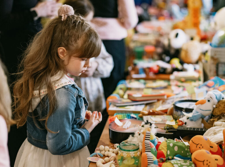 Zdjęcie przedstawia dziewczynkę, która przygląda się kolorowym zabawkom.