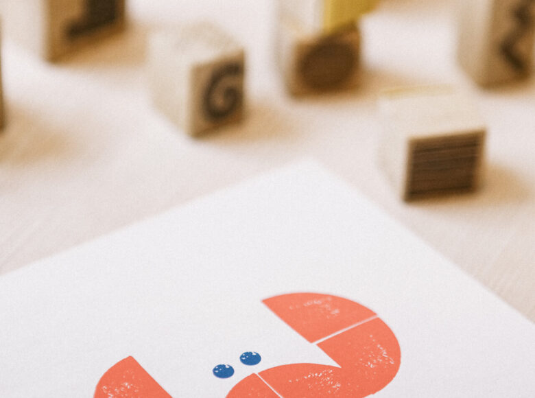 Zdjęcie przedstawia drewniane stemple ułożone w kilku rzędach na stole. Na blacie znajduje się również kartka papieru z rysunkiem przedstawiającym kraba.