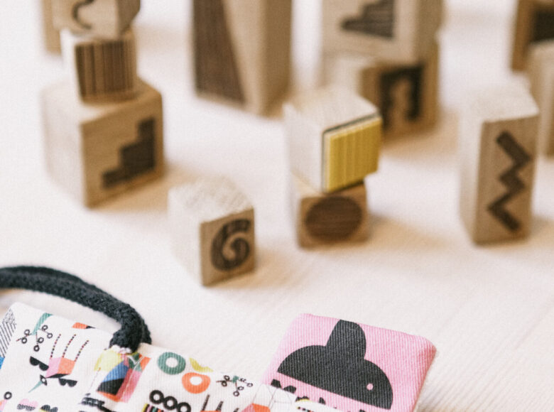 Zdjęcie przedstawia drewniane stemple z różnymi wzorami. Klocki lezą na stole, ustawione w kilku rzędach. Na drewnianym blacie znajduje się również torba z kolorowymi wzorami.