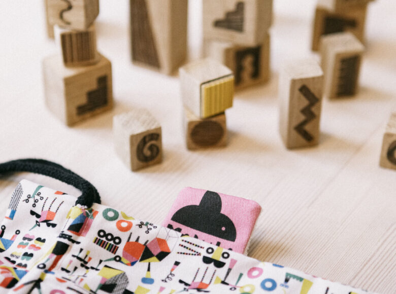 Zdjęcie przedstawia drewniane stemple z różnymi wzorami. Klocki lezą na stole, ustawione w kilku rzędach. Na drewnianym blacie znajduje się również torba z kolorowymi wzorami.