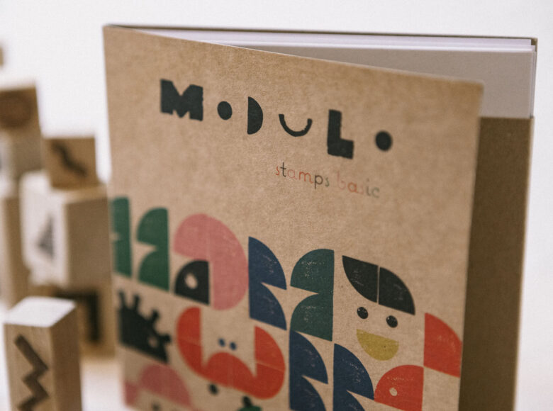 Na zbliżeniu okładka książki. Na okładce znajduje się grafika, wykonana za pomocą kolorowych stempli.