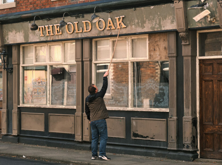 Mężczyzna stojący przed kamienicą, poprawia szyld baru.