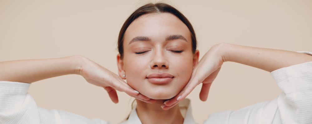 Zdjęcie przedstawia kobietę. Ma zamknięte oczy i zrelaksowany wyraz twarzy. Ręce trzyma pod brodą.