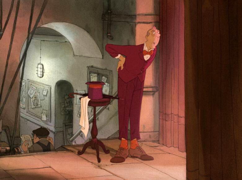 Kadr z filmu animowanego. Wnętrze. Na zapleczu sceny stoi mężczyzna w ciemnoróżowym garniturze i z czerwoną muchą. Obok niego stoi mały, okrągły stoliczek, na którym leży cylinder, parasol i chusta. Mężczyzna wygląda za kurtynę z otwartymi ustami.