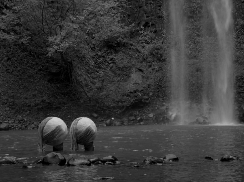 Czarno-białe zdjęcie. Przedstawia jezioro i wodospad. W jeziorze znajdują się dwie rzeźby w kształcie kul.