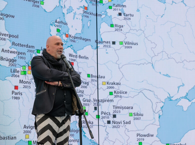 Dyrektor Centrum Kultury w Lublinie przemawia do mikrofonu. Za nim mapa Europu z zaznaczonymi miastami, które do tej pory otrzymały tytuł Europejskiej Stolicy Kultury.