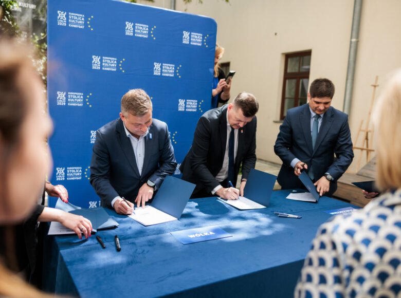 Wirydarz Centrum Kultury w Lublinie. Za stołem stoją trzej mężczyźni w garniturach i podpisują dokumenty.