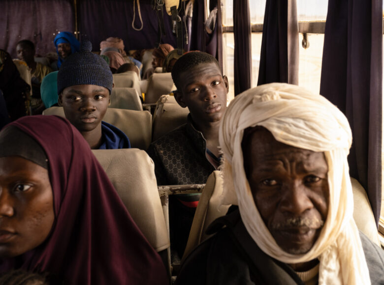 Kolorowa fotografia przedstawia czarnoskóre osoby, jadące autobusem. Znajdują się tu zarówno młodzi jak i starsi ludzie.