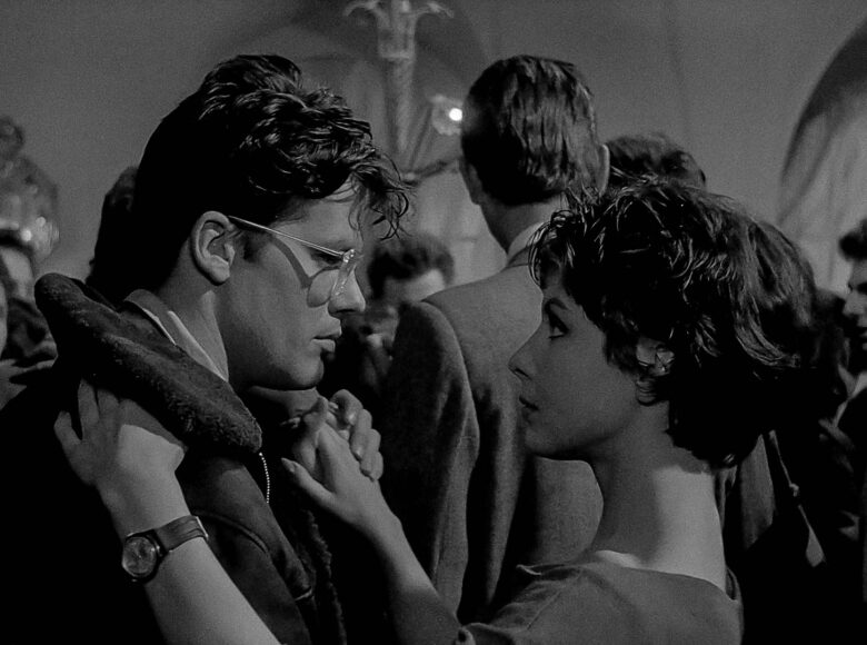 Czarnobiały fotos z filmu przedstawia parę - mężczyznę i kobietę tańczących w tłumie innych ludzi. Wpatrują się w swoje oczy.