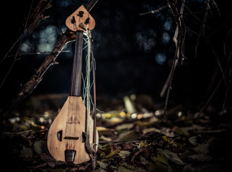 Kolorowa, ale ciemna fotografia przedstawia jasnobrązowy, stary instrument w lesie.
