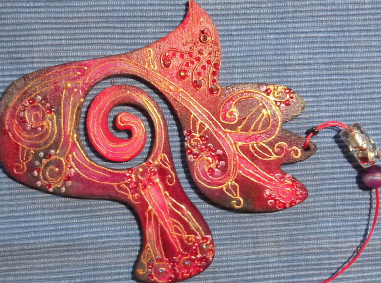 Zdjęcie przedstawia czerwono złotą, płaską, pozawijaną figurę z czerwonym sznureczkiem.