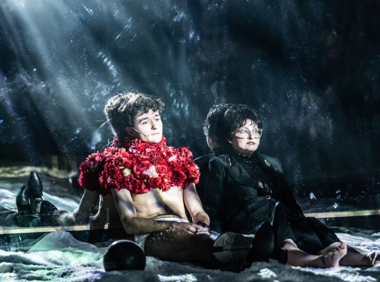 Kobieta i mężczyzna siedzą na podłodze. Oboje są oparci o lustrzaną ścianę, dookoła nich rozrzucony śnieg.