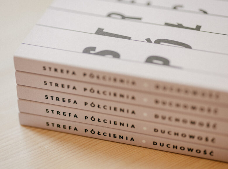 Fotografia przedstawia ułożone na sobie białe książki o tytule "Strefa półcienia".