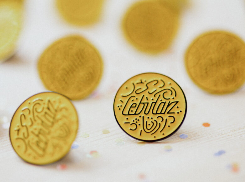 Kolorowa fotografia przedstawia żółte przypinki z czarnym napisem "Cebularz", które same w sobie przypominają wyglądem cebularze.