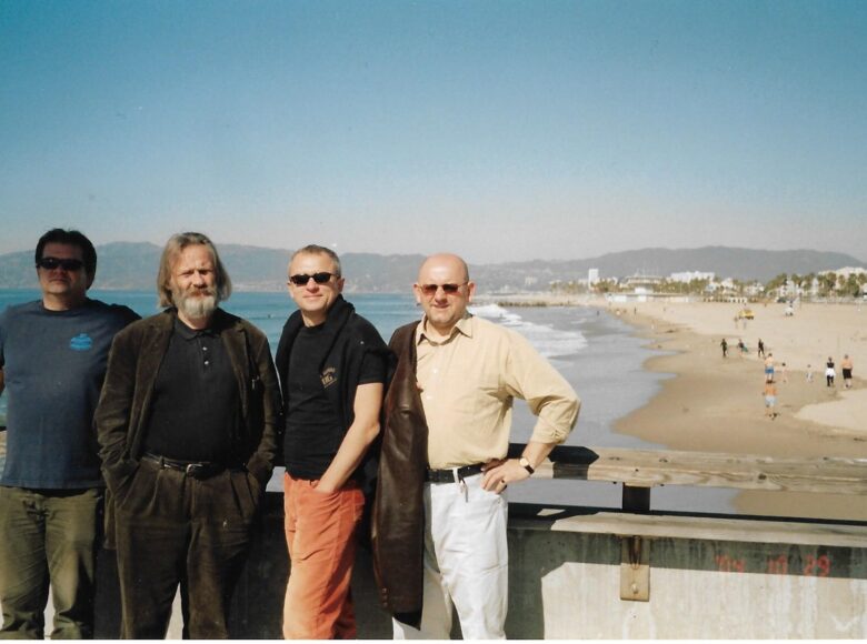 Na fotografii czterej mężczyźni. Za nimi plaża i morze. Jest słoneczny dzień.