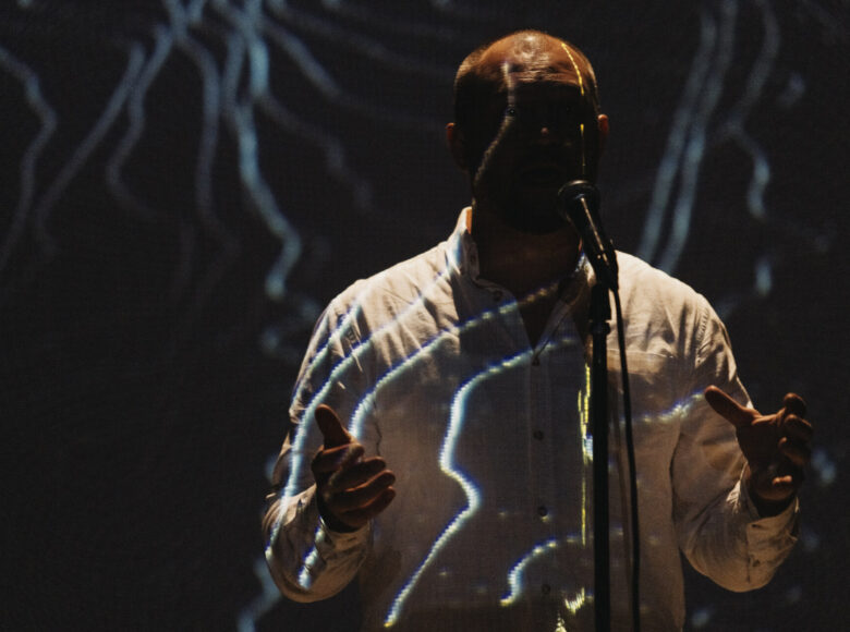 Na ciemnej scenie mężczyzna śpiewający do mikrofonu.