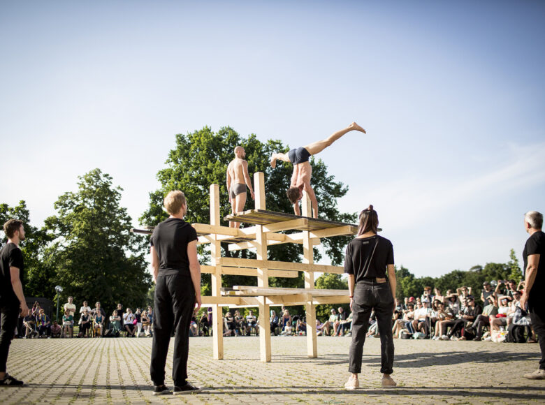 Jasny dzień.. Występ akrobatów na miejskim placu. w tle publiczność. Na ostatnim planie drzewa.