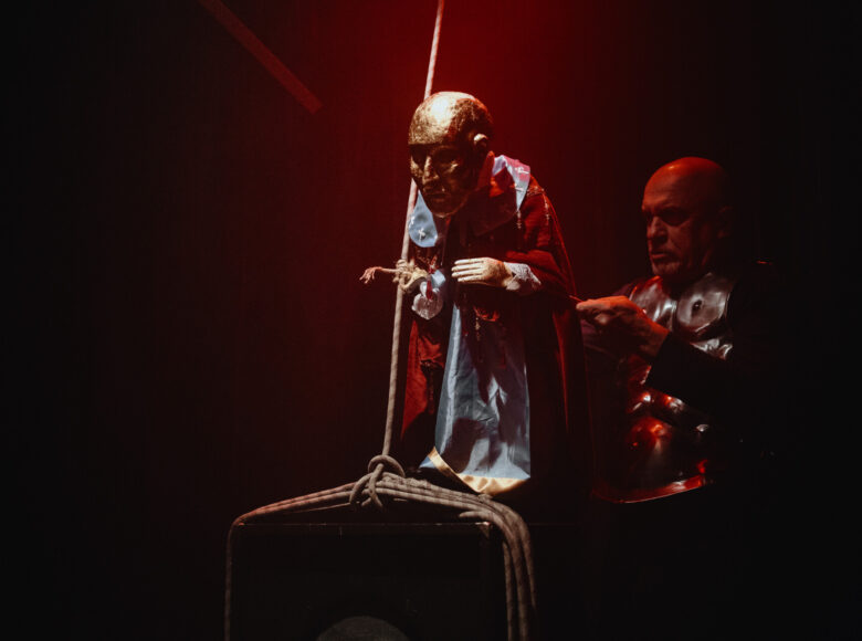 Przedstawienie teatralne. W ciemnej przestrzeni aktor poruszający lalką teatralną.