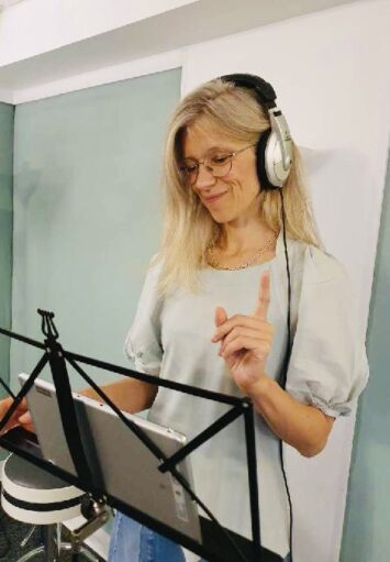 W jasnym wnętrzu kobieta ze słuchawkami na uszach.