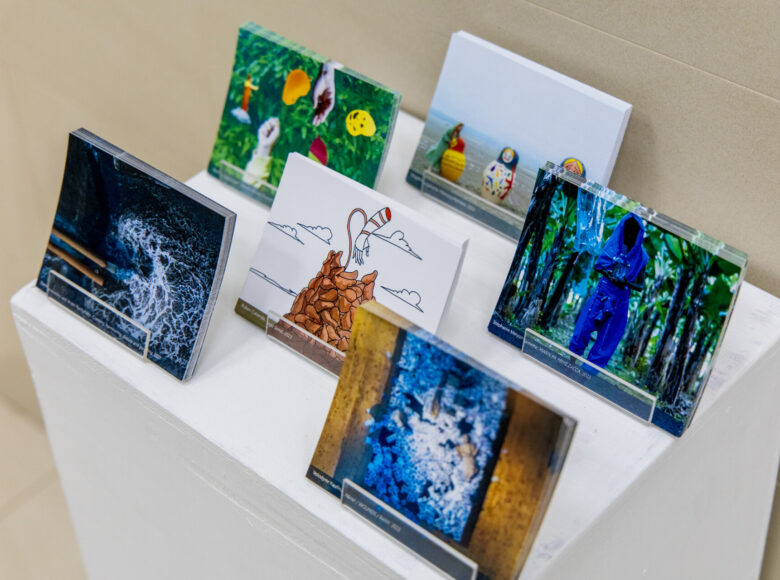 Niedookreślone pomieszczenie. Zbliżenie na mały postument, na którym znajdują się pocztówki ułożone w stojakach.