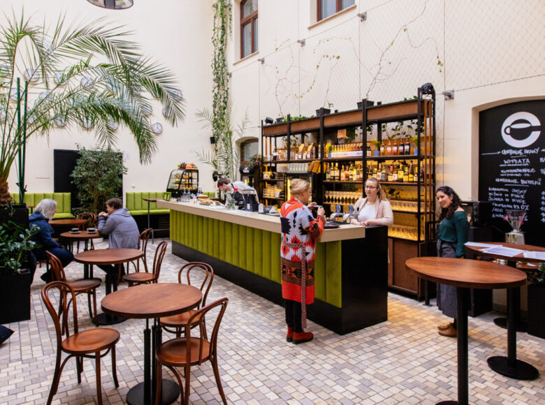 Wnętrze kawiarni w Centrum Kultury w Lublinie. Za barem kilka osób. Dookoła stoliki. Przy jednym z nich siedzi dwóch mężczyzn.