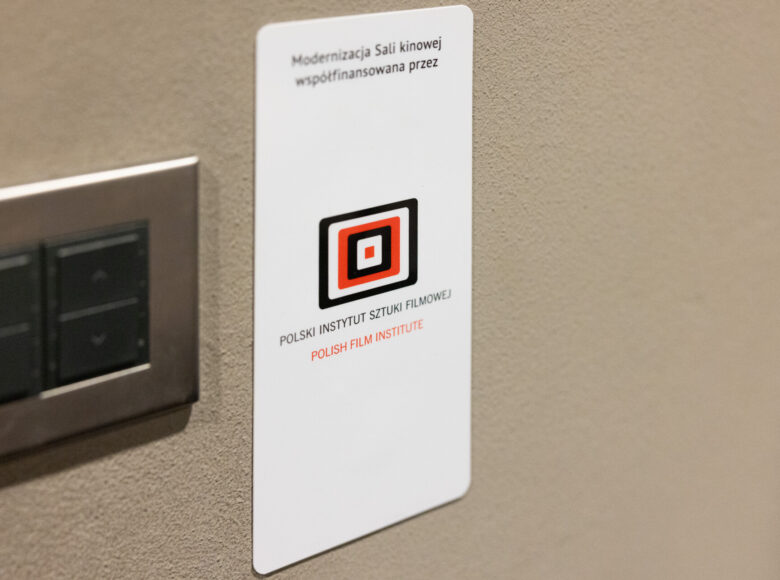 Zbliżenie na wiszącą na ścianie tabliczkę z napisem: "Modernizacja sali kinowej współfinansowana przez Polski Instytut Sztuki Filmowej."
