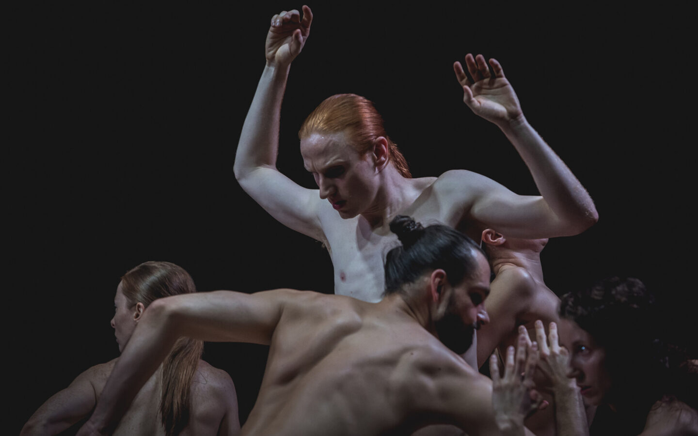 Spektakl teatralny. Zbliżenie na grupę nagich osób w dynamicznych pozach.