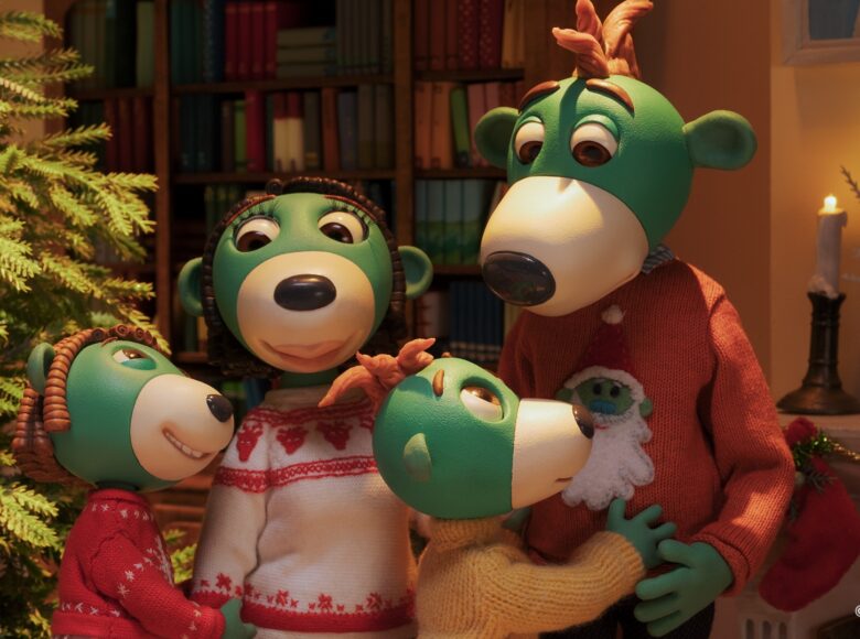 Kadr z filmu animowanego. W pokoju choinka i półki z książkami. Na pierwszym planie rodzina nieznanych zielonych ssaków ubranych w swetry.