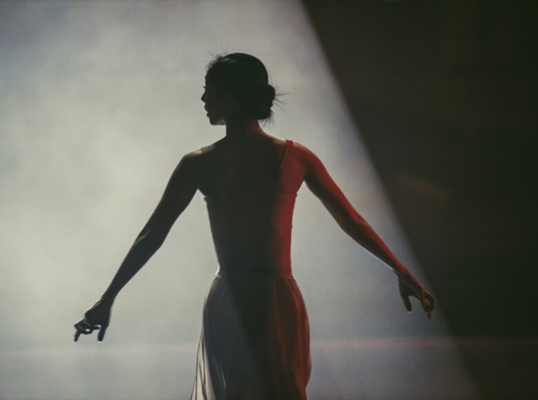 Tancerka w baletowej pozie, oświetlona padającym z góry światłem reflektora.