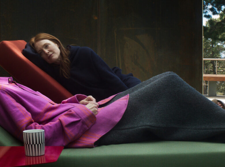 Na szezlongach leżą dwie kobiety. W tle fragment ściany i widok na drzewa.